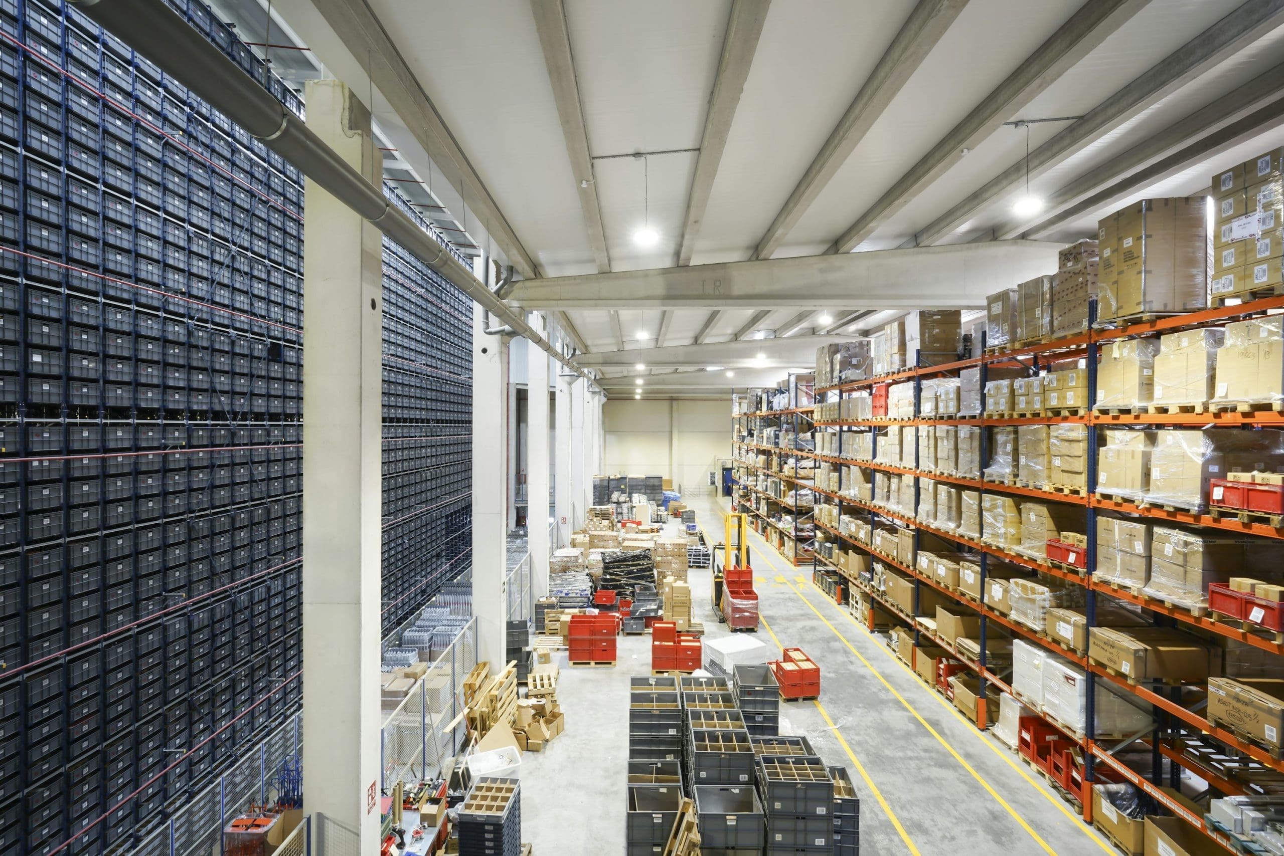 A high view of an organized warehouse with plenty of items across the walls and shelves, with stacks of pallets in the middle